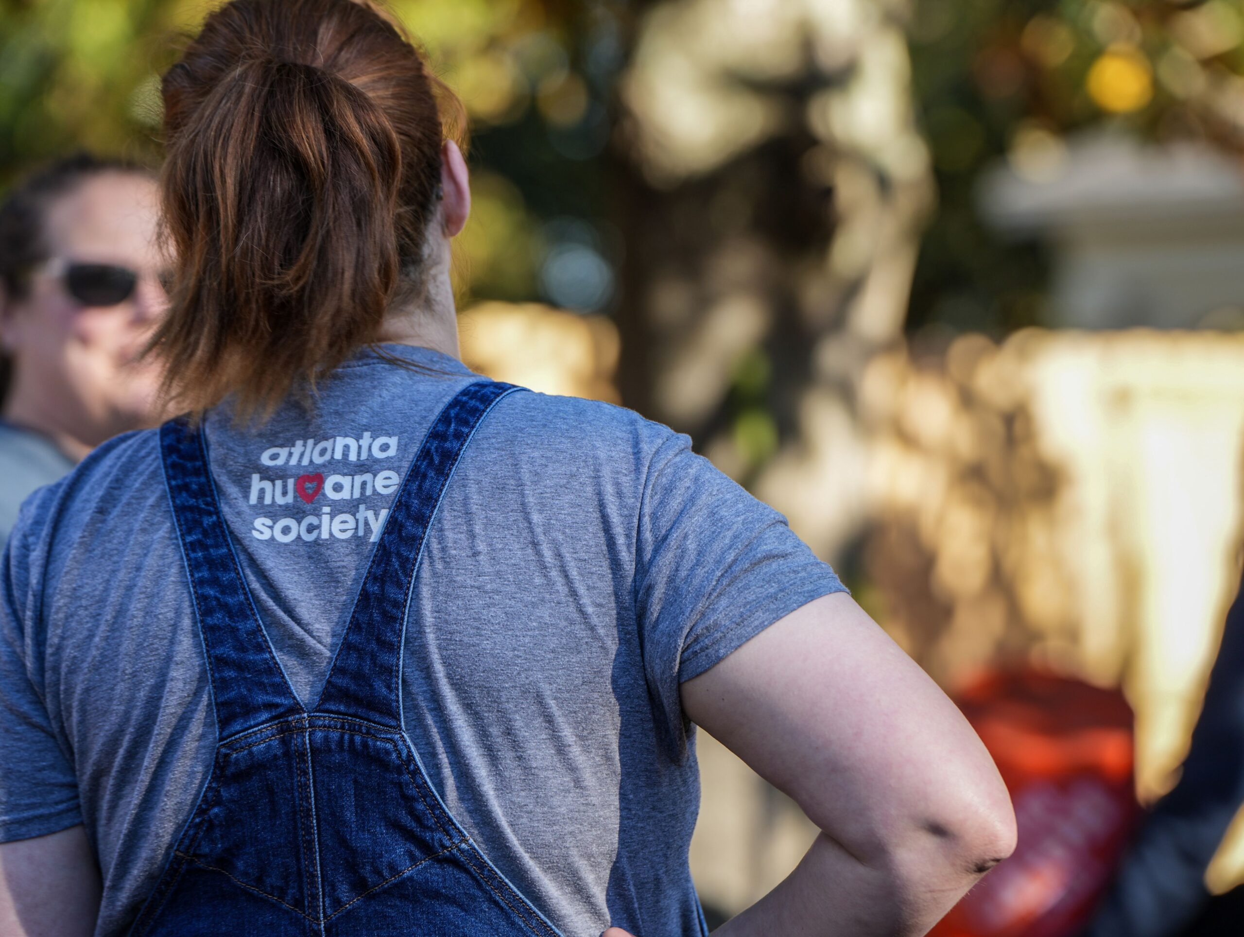 A woman stands with her back to the camera. Her shirt reads "Atlanta Humane Society".